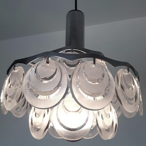 May include: A silver pendant light fixture with a cluster of overlapping, translucent, circular discs. The discs are arranged in a flower-like shape.