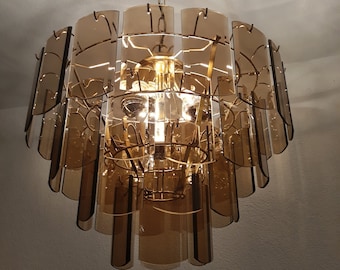 May include: A brown glass chandelier with a geometric design. The chandelier has multiple tiers of glass panels that are arranged in a staggered pattern. The chandelier is hanging from a chain.
