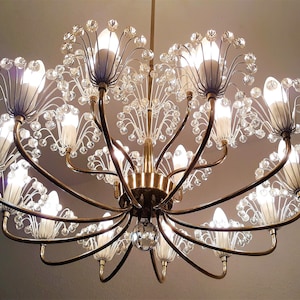Op de afbeelding: Een gouden kroonluchter met heldere kristallen accenten en witte matte gloeilampen. De kroonluchter heeft een bloemmotief met meerdere armen.