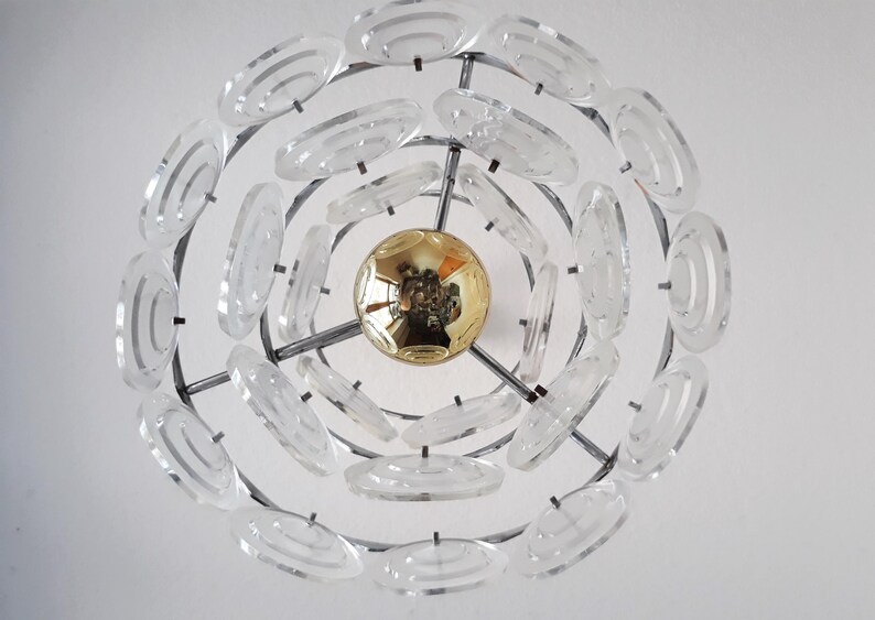 May include: A modern chandelier with a circular design featuring multiple clear glass rings. The chandelier has a gold-colored center piece.