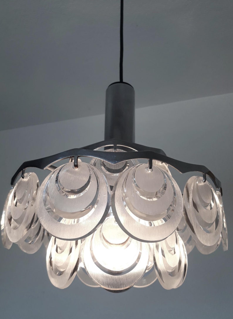 May include: A silver pendant light fixture with a cluster of overlapping, translucent, circular discs. The discs are arranged in a flower-like shape.