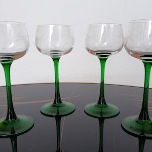 May include: Four clear glass wine glasses with green stems and bases. The glasses are arranged in a row on a black surface.