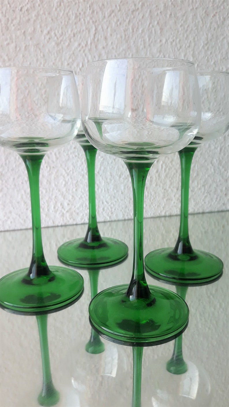 K&ouml;nnte beinhalten: Vier klare Weingl&auml;ser aus Glas mit gr&uuml;nen Stielen und F&uuml;&szlig;en. Die Gl&auml;ser sind in einer Reihe auf einer wei&szlig;en Oberfl&auml;che angeordnet.