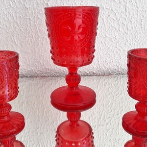 Puede incluir: Tres copas de vidrio rojo con un diseño decorativo. Las copas tienen una base redonda y un tallo.