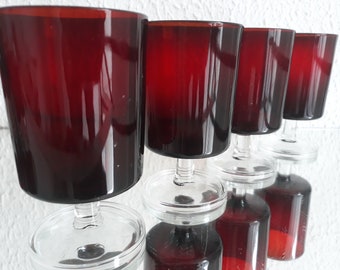 May include: A set of six vintage wine glasses. The glasses have a deep red bowl and a clear stem and base. The glasses are arranged in a row, reflecting on a mirrored surface.