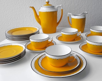 May include: A yellow and white tea set with a teapot, creamer, sugar bowl, and four cups and saucers. The set has a black trim and a scalloped edge.