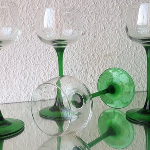 K&ouml;nnte beinhalten: Vier klare Weingl&auml;ser aus Glas mit gr&uuml;nen Stielen und F&uuml;&szlig;en. Die Gl&auml;ser sind auf einer reflektierenden Oberfl&auml;che angeordnet.