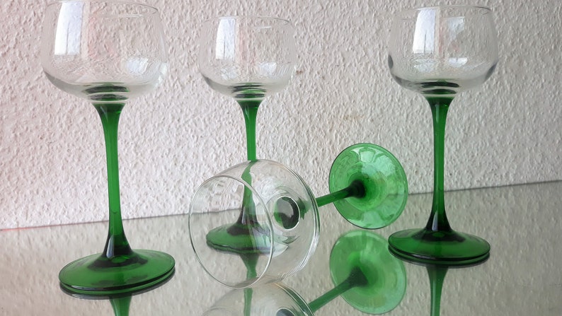K&ouml;nnte beinhalten: Vier klare Weingl&auml;ser aus Glas mit gr&uuml;nen Stielen und F&uuml;&szlig;en. Die Gl&auml;ser sind auf einer reflektierenden Oberfl&auml;che angeordnet.