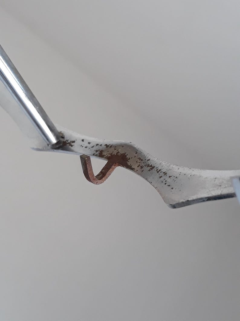 May include: Close-up of a silver metal hook with a rusty brown finish. The hook is bent at a 90-degree angle and has a small loop at the end.