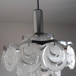 May include: A chrome and clear glass pendant light fixture with a modern design. The light features multiple circular glass shades that are layered and have a frosted finish.