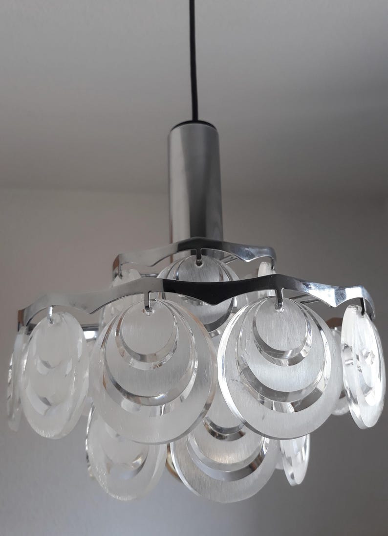 May include: A chrome and clear glass pendant light fixture with a modern design. The light features multiple circular glass shades that are layered and have a frosted finish.