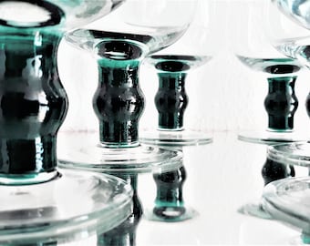 May include: Set of six clear glass stemmed goblets with a dark green base. The goblets are arranged in a row, with the bases of the goblets overlapping.
