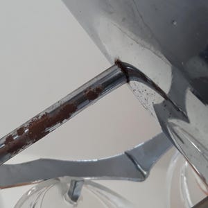 May include: Close-up of a chrome-plated metal light fixture with a rusty metal arm. The fixture has a clear glass shade.