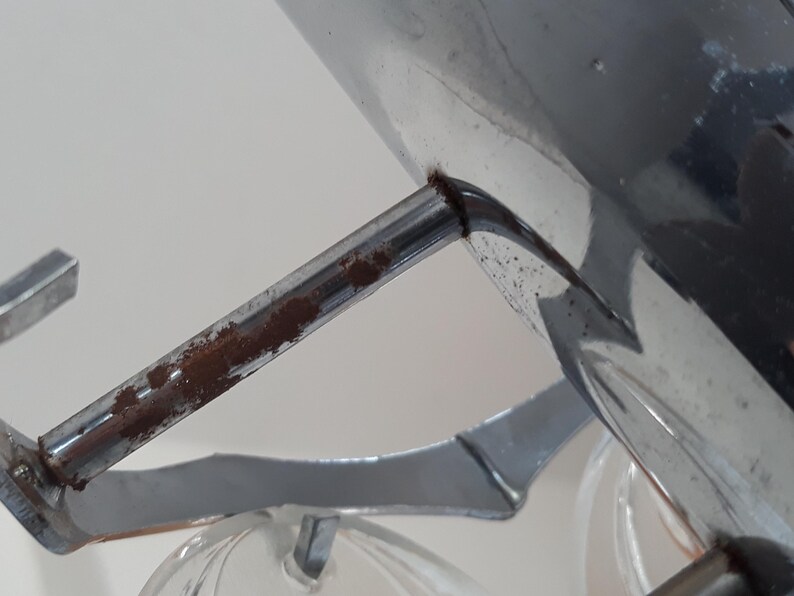 May include: Close-up of a chrome-plated metal light fixture with a rusty metal arm. The fixture has a clear glass shade.