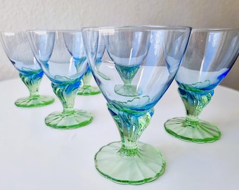 Könnte beinhalten: Ein Set aus fünf Glaspokalen mit einer hellblauen, transparenten Kuppa, die in einen leuchtend grünen Stiel und einen breiten, geriffelten runden Fuß übergeht. Jedes Stück zeigt einen deutlichen Farbverlauf vom oberen Rand bis zum Fuß.