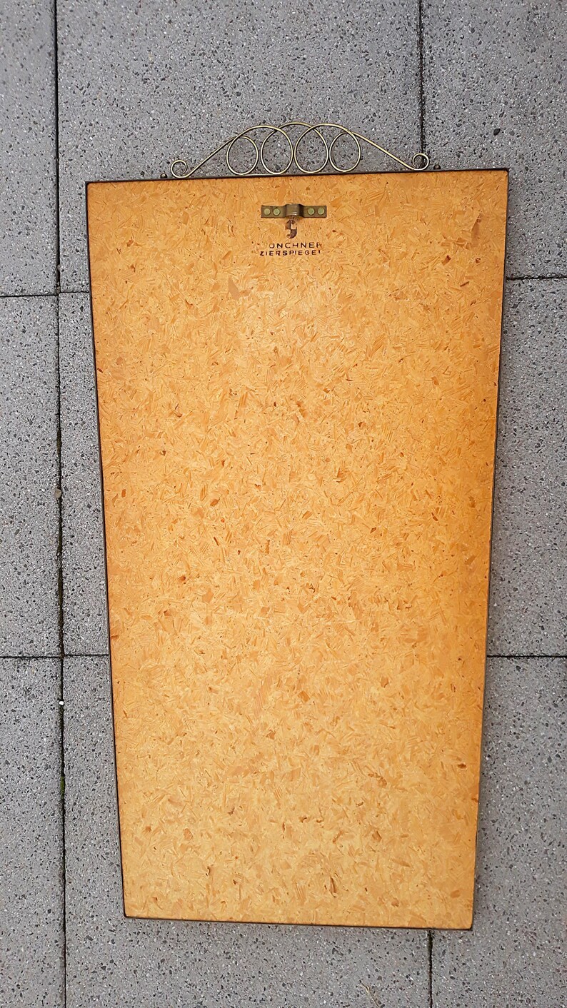 May include: A rectangular wooden framed mirror with a decorative metal top. The mirror's backing is a light brown color with a textured surface. The text "UNCHNER ZIERSPIEGEL" is visible on the back.