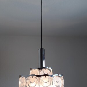 May include: A chrome and glass pendant light fixture with a circular design. The light fixture has multiple layers of clear glass circles that create a unique and modern look.