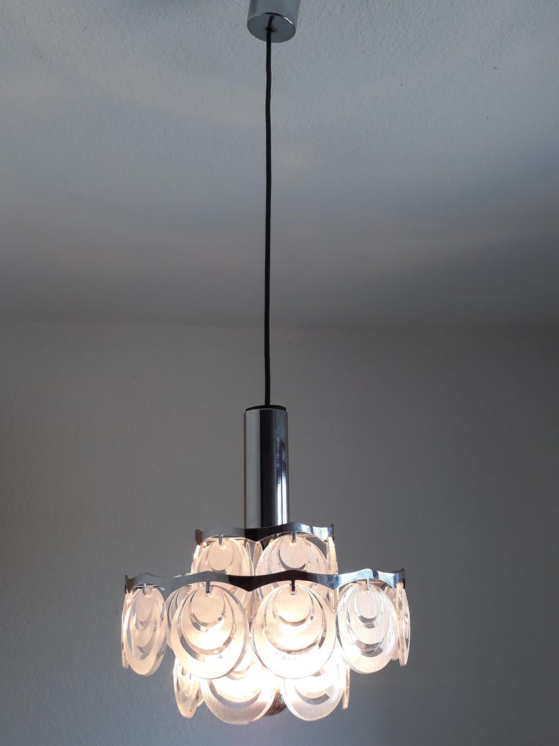 May include: A chrome and glass pendant light fixture with a circular design. The light fixture has multiple layers of clear glass circles that create a unique and modern look.