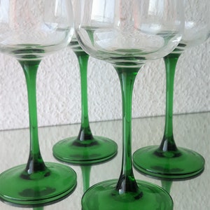 K&ouml;nnte beinhalten: Vier klare Weingl&auml;ser aus Glas mit gr&uuml;nen Stielen und F&uuml;&szlig;en. Die Gl&auml;ser sind in einer Reihe auf einer wei&szlig;en Oberfl&auml;che angeordnet.