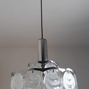 May include: A chrome and glass pendant light fixture with a circular design. The light fixture has multiple layers of clear glass circles that are stacked on top of each other.