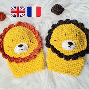 以下が含まれることがあります： 茶色の毛糸でたてがみ、黄色の毛糸で体を作った、手編みのライオンのぬいぐるみが2つ。1つのライオンは茶色の毛糸のしっぽ、もう1つのライオンはオレンジ色の毛糸のしっぽです。