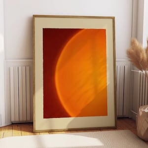 May include: Abstract art print featuring a vibrant orange and yellow gradient against a deep red background. The artwork is framed in a light wood frame and leans against a white wall. The artwork evokes a sense of warmth and energy.
