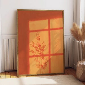 May include: A rectangular framed wall art print featuring a warm orange and yellow gradient background. The image displays a dark silhouette of a leafy plant branch cast by a window frame, creating a grid pattern of shadows across the surface.