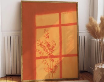 May include: A rectangular framed wall art print featuring a warm orange and yellow gradient background. The image displays a dark silhouette of a leafy plant branch cast by a window frame, creating a grid pattern of shadows across the surface.