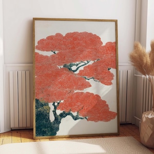 May include: A framed art print featuring a stylized tree with vibrant red foliage and dark green branches. The artwork is set against a white background, encased in a light brown wooden frame, and displayed indoors.