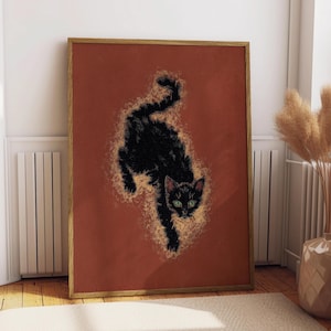 May include: A framed art print featuring a black cat with green eyes against a rust-colored background. The cat is depicted in a stylized, dynamic pose, surrounded by a golden, textured effect. The artwork is in a wooden frame.