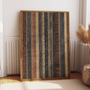 May include: A framed artwork with a vertical striped pattern in shades of brown, beige, and black. The artwork has a wooden frame and is leaning against a white wall. The stripes include decorative patterns.