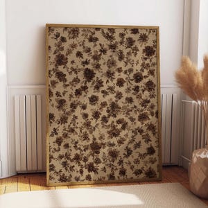 May include: A framed floral print featuring a repeating pattern of brown flowers on a beige background. The artwork is displayed in a room with a neutral color palette, including a beige rug and a vase with dried plants.