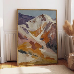 Peut inclure: Peinture encadrée d'un paysage de montagne. L'œuvre représente une montagne enneigée avec des tons orange, jaune et violet. La peinture est dans un cadre en bois et est posée contre un mur blanc. L'œuvre est exposée sur un sol en bois.