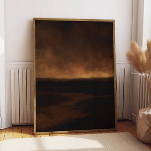 Puede incluir: Pintura de paisaje abstracto enmarcada en tonos marrones y dorados. La obra presenta un cielo oscuro y melancólico sobre una masa terrestre más oscura, creando una sensación de profundidad y atmósfera. El marco es de madera natural cálida.