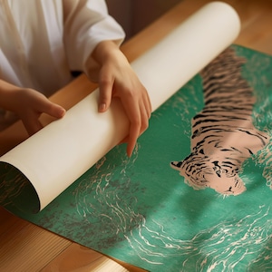 以下が含まれることがあります： 緑色の背景に虎のイラストが描かれたポスターが丸められています。虎はピンクと黒で描かれ、水のようなデザインが施されています。ポスターは木製のテーブルの上で広げられています。
