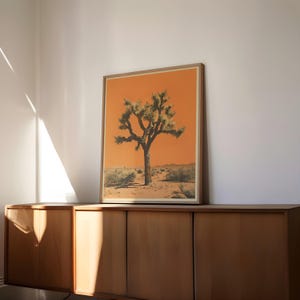 May include: A framed print of a Joshua tree in a desert landscape. The tree is green and the background is a vibrant orange.