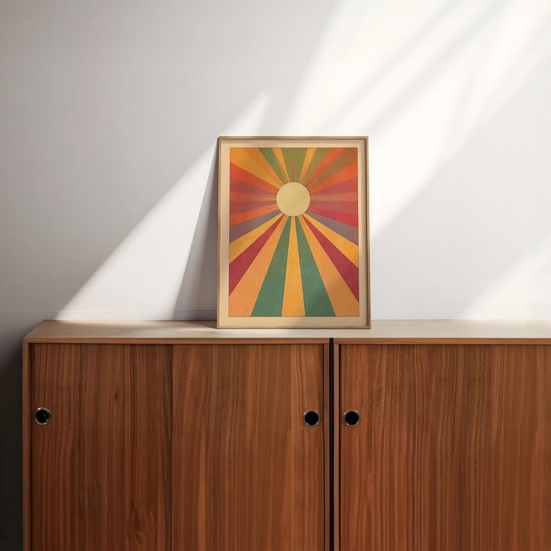 Op de afbeelding: Een ingelijst afdruk van een retro zonnestralenontwerp met een gele zon in het midden en stralende lijnen in rood, oranje, geel, groen en blauw.