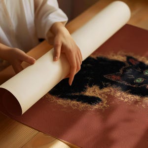 May include: A rolled-up, off-white canvas print being unrolled to reveal a black cat illustration with green eyes and red accents. The cat is set against a reddish-brown background with gold-colored accents.