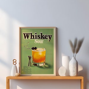 May include: A framed print of a vintage whiskey sour cocktail advertisement. The print features a green background with the text "Whiskey Sour" in black lettering. A glass of whiskey sour with a cherry garnish is depicted in the centre of the print.