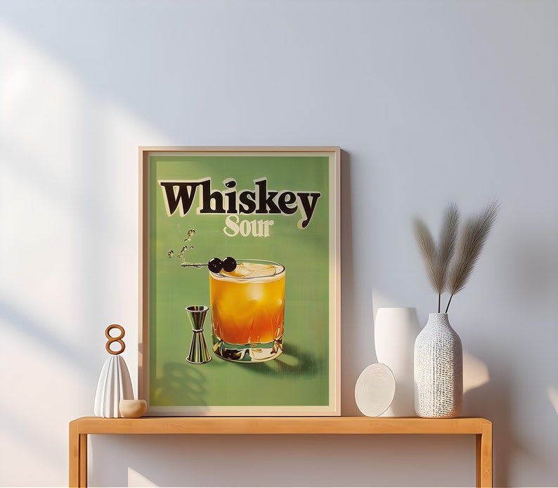 May include: A framed print of a vintage whiskey sour cocktail advertisement. The print features a green background with the text "Whiskey Sour" in black lettering. A glass of whiskey sour with a cherry garnish is depicted in the centre of the print.