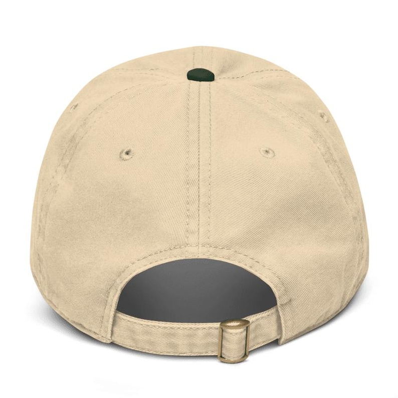 May include: A beige baseball cap with a curved brim, adjustable strap, and a dark green button on top. The cap is made of a soft, textured fabric.