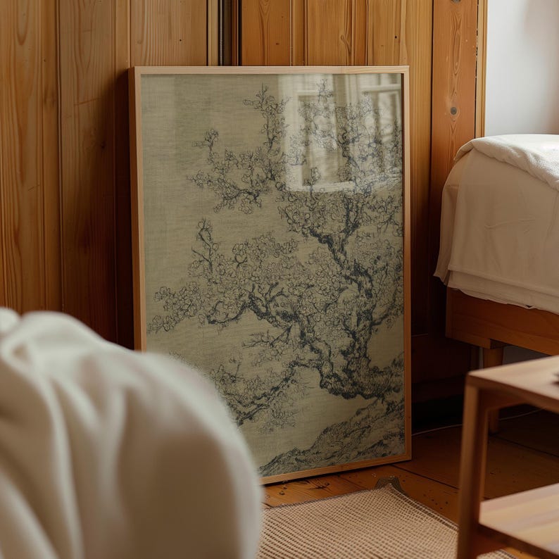 Puede incluir: Una obra de arte enmarcada que presenta una ilustraci&oacute;n detallada de un &aacute;rbol en flor. La obra de arte est&aacute; en un marco de madera clara y se apoya contra una pared de madera. La ilustraci&oacute;n del &aacute;rbol est&aacute; en tonos grises y negros, con ramas y flores delicadas.