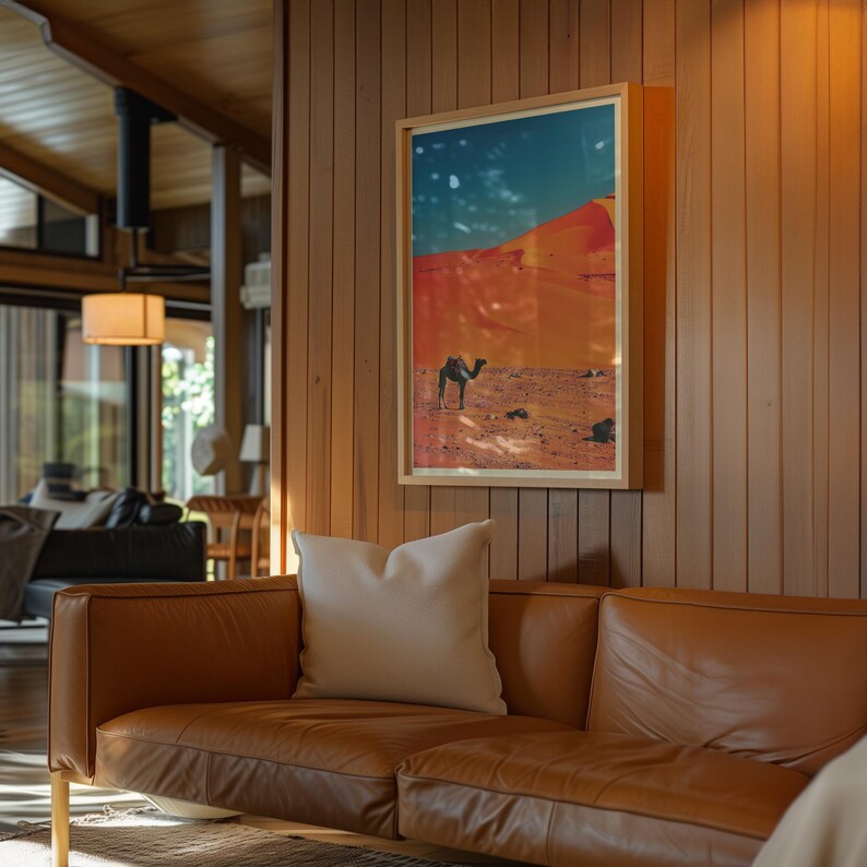 K&ouml;nnte beinhalten: Ein braunes Ledersofa mit zwei wei&szlig;en Kissen vor einer Holzvert&auml;felung. An der Wand h&auml;ngt ein gerahmtes Bild eines Kamels, das durch eine W&uuml;stenlandschaft geht.
