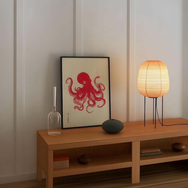 May include: A wooden console table with a framed red octopus print, a glass vase, and a small, round, dark green vase. A paper lantern lamp with a black metal base sits on the right. The lamp is lit, casting a warm glow.