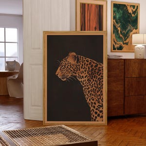 May include: A framed print of a leopard in profile against a black background. The leopard is brown and gold with black spots. The frame is a light wood color.
