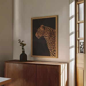 May include: A framed print of a leopard with a dark background. The leopard is facing to the left and has a brown and black spotted pattern.
