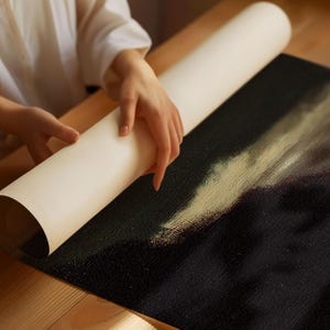 以下が含まれることがあります： 人が白黒のキャンバスプリントを展開しています。プリントは、薄い黄色と白の背景に人物の絵が描かれています。