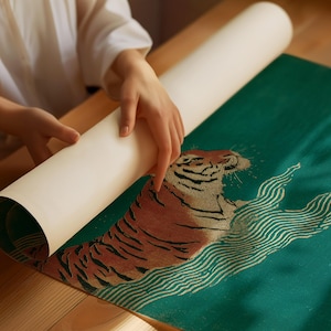 May include: A rolled-up print featuring a tiger design is being unrolled. The tiger is depicted in shades of brown and tan against a teal background with white wave-like patterns. The print is on a wooden surface.