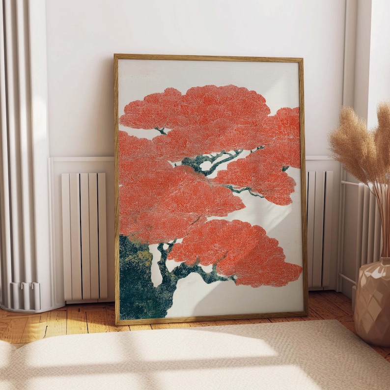 May include: A framed art print featuring a stylized tree with vibrant red foliage and dark green branches. The artwork is set against a white background, encased in a light brown wooden frame, and displayed indoors.