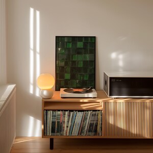 May include: A wooden media console with a record player, a framed green artwork, and a spherical lamp. The console has a section for vinyl records and a black and white stereo component. The room is lit by natural light.